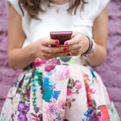 close-up of woman's hands holding a smartphone standing in front of purple brick wall